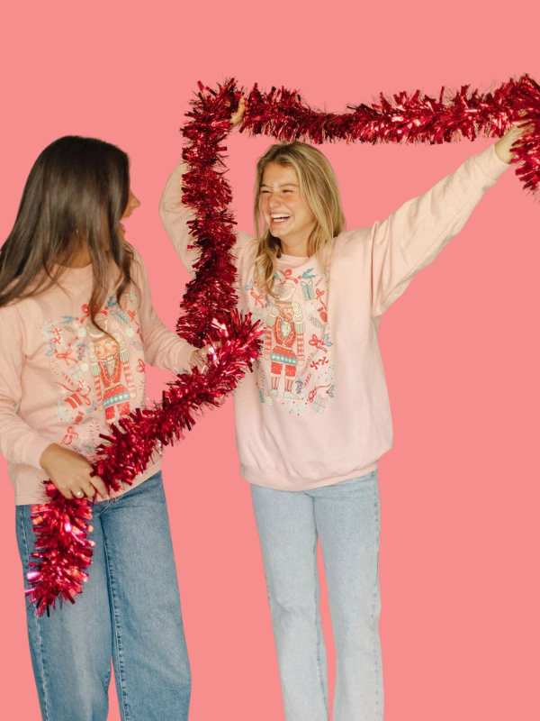 Two people holding red tinsel against a pink background