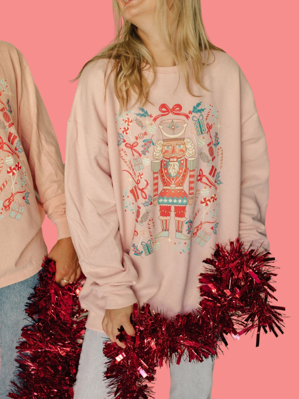 Person wearing a pink sweatshirt with a robot design, holding red tinsel against a pink background