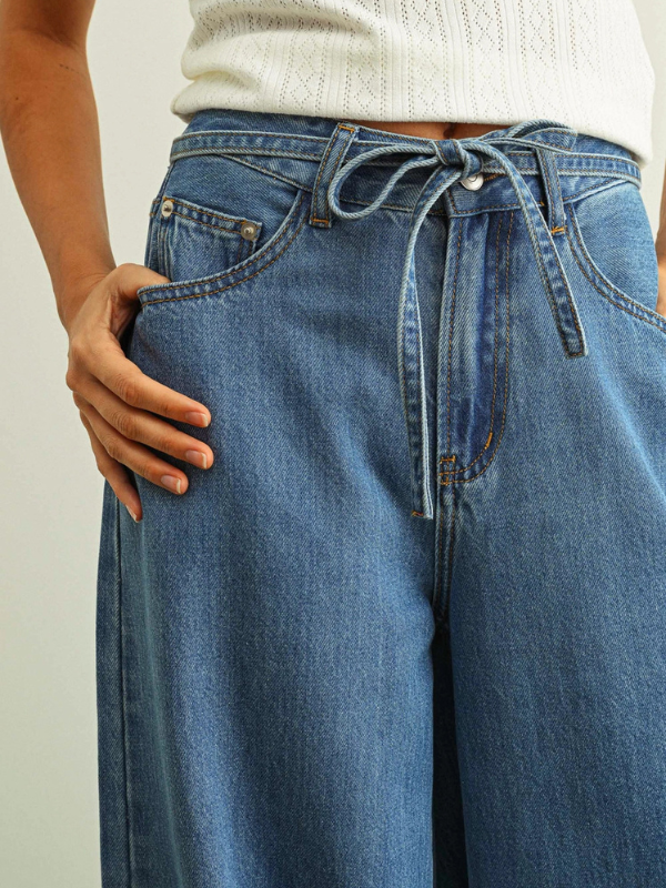 Person wearing blue wide-leg jeans with a white sweater underneath on a plain background