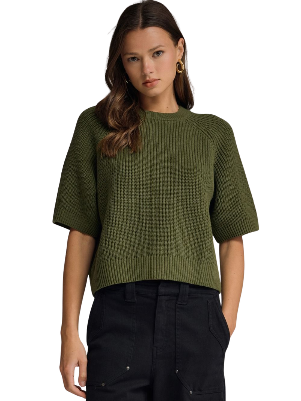 A woman wearing a cropped, short-sleeve ribbed knit sweater in olive green, paired with black pants, against a plain white background.
