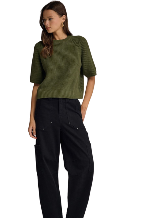 A woman modeling a short-sleeve olive green ribbed knit top paired with black pants, photographed against a plain white background.