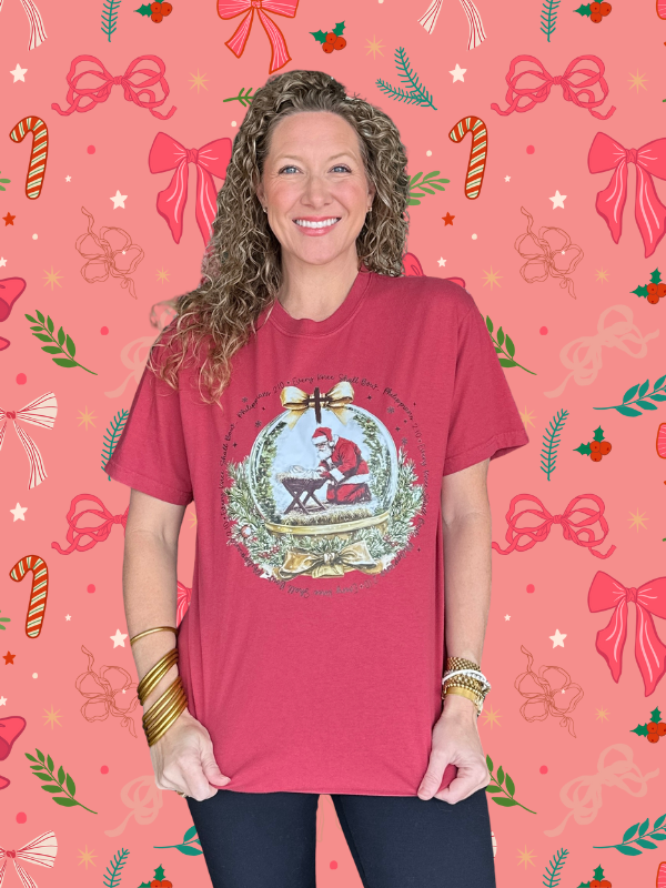 Woman wearing a red t-shirt with a Christmas design on a pink background with festive patterns.