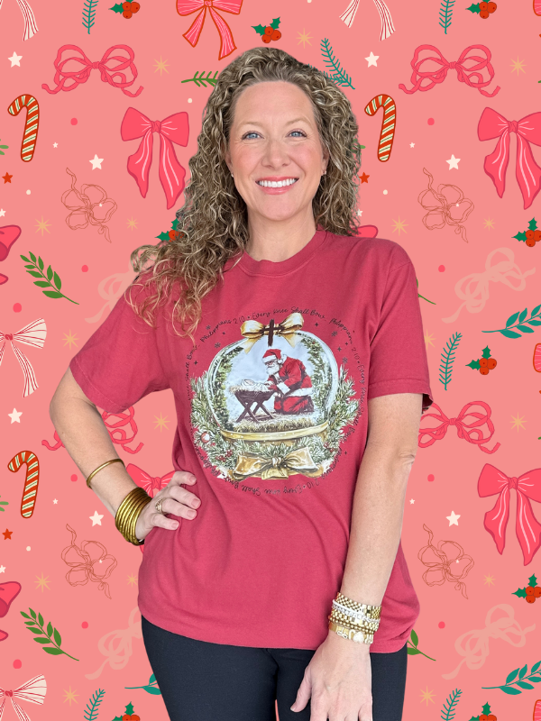 Woman wearing a red t-shirt with a Christmas design on a pink background with festive patterns.