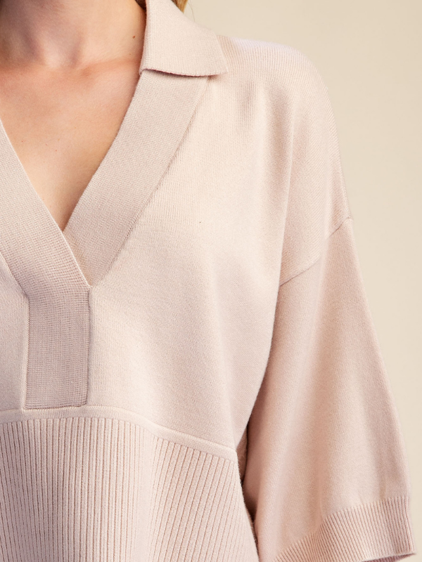 Close-up of a model wearing a light beige knit top with a V-neck, wide collar, and ribbed sleeve panels.