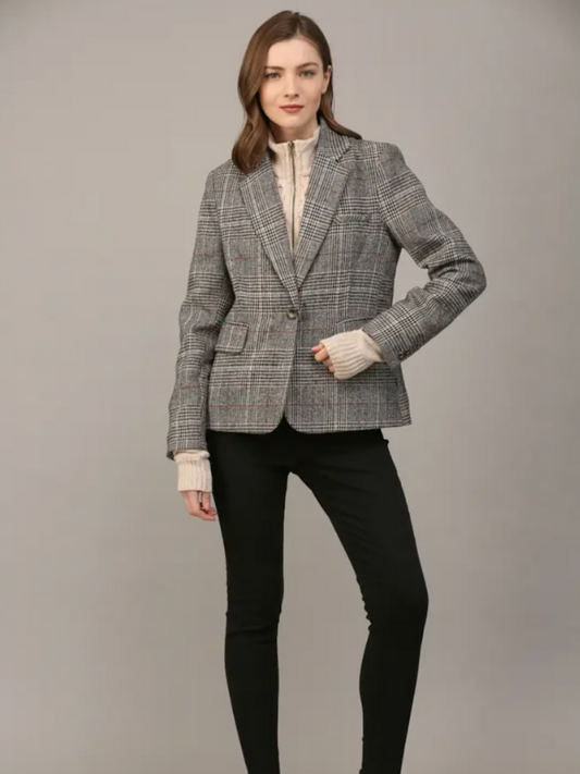 Woman wearing a gray checkered blazer over a cream top with black pants on a gray background