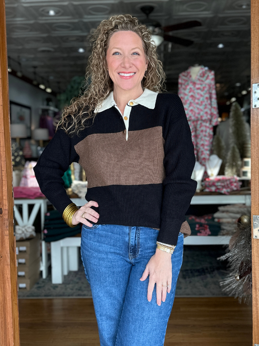 Woman wearing a black and brown sweater with blue jeans standing in a store.
