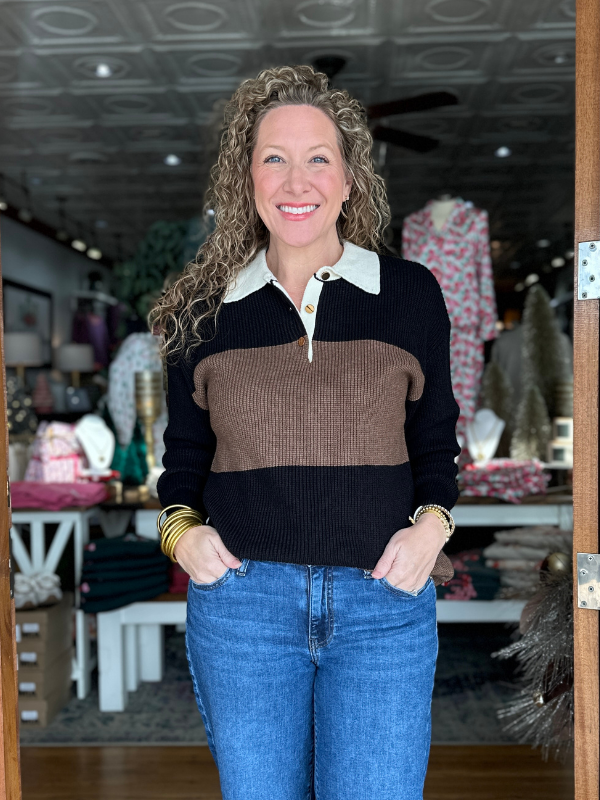 Woman wearing a black and brown sweater with blue jeans in a store setting