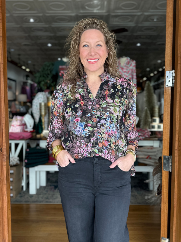 Woman wearing a floral blouse and dark jeans standing in a store.