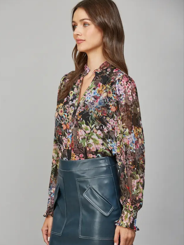Woman wearing a floral blouse and blue leather skirt against a gray background