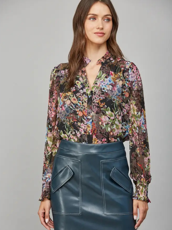 Woman wearing a floral blouse and blue leather skirt against a gray background