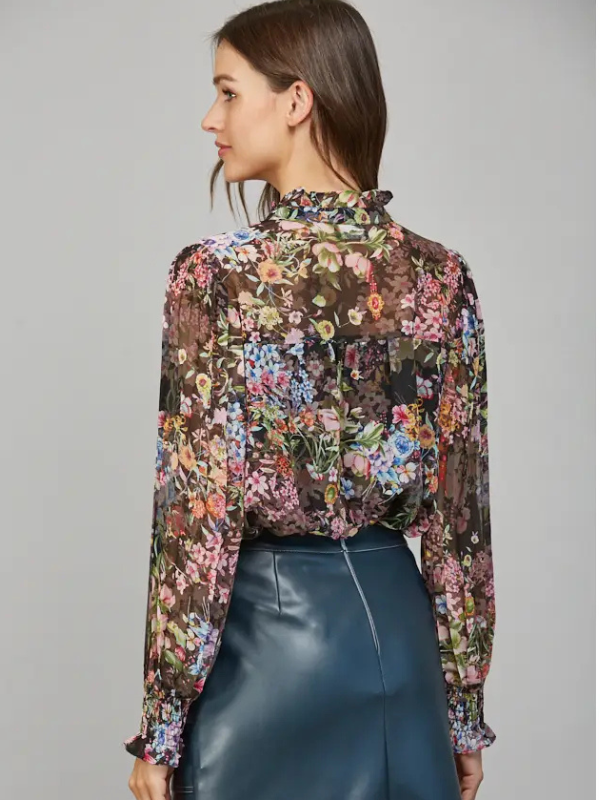 Woman wearing a floral blouse with long sleeves and a high collar on a gray background