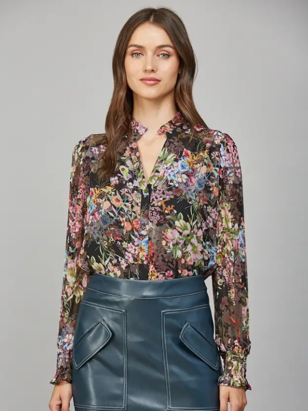 Woman wearing a floral blouse and blue leather skirt against a gray background