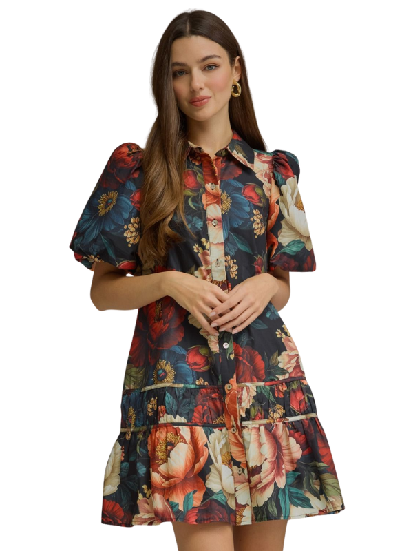 A woman modeling a short puff-sleeve mini dress with a colorful floral print on a dark navy background, featuring red, pink, orange, and cream flowers.