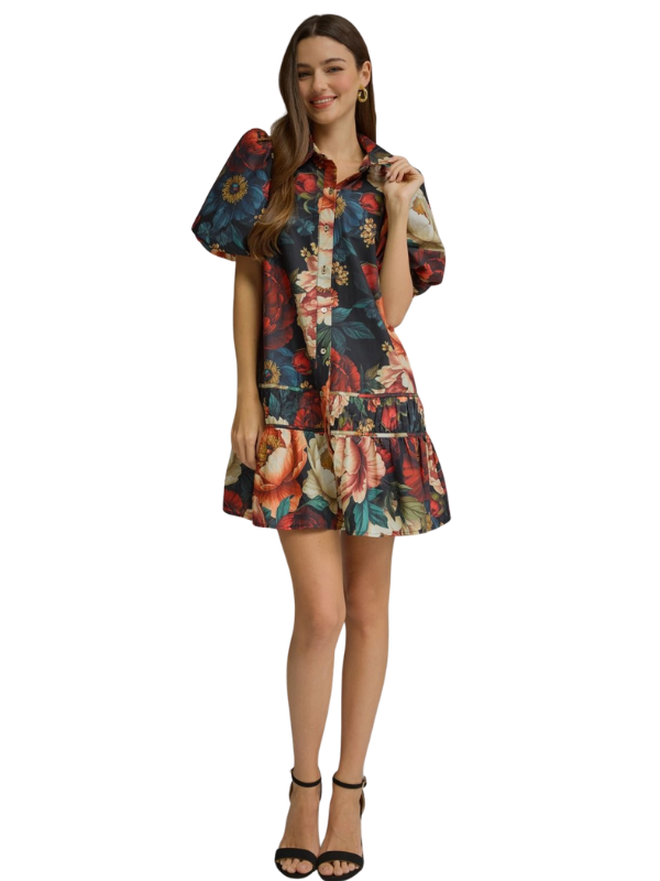 A woman modeling a short-sleeve button-up shirt dress with a colorful floral print, featuring puff sleeves and a tiered ruffle hem, set against a plain white background.