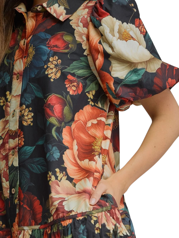 Close-up of a floral print dress with a dark navy base and large orange, red, cream, and green flowers, worn by a model with one hand in the pocket.