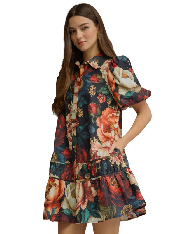 A woman modeling a short-sleeve floral dress with puff sleeves, a button-up front, and a tiered ruffled hem against a plain white background.