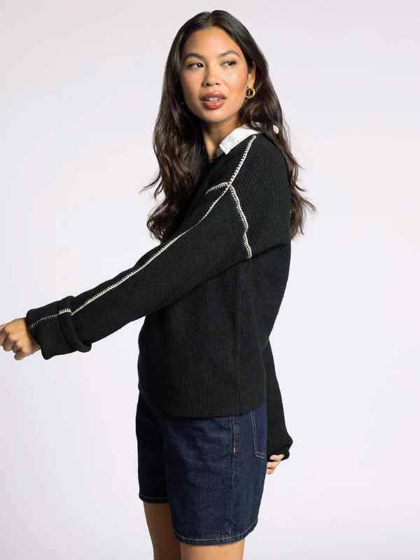 Woman wearing a black sweater with white trim on a plain background