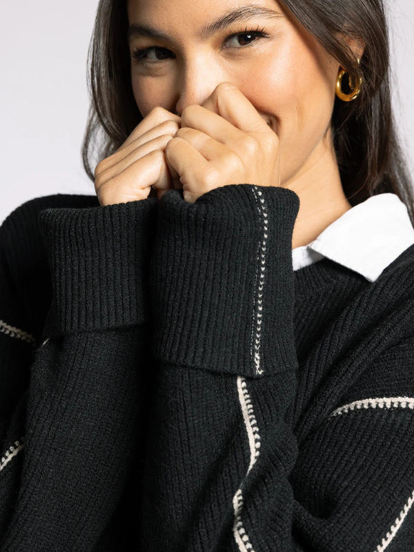 Woman wearing a black sweater with white trim on a plain background