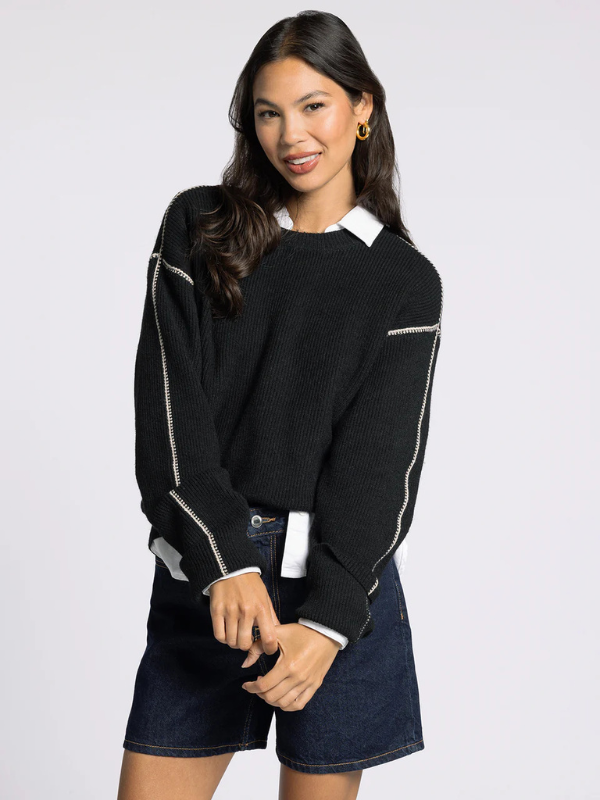 Woman wearing a black sweater with white accents on a plain background
