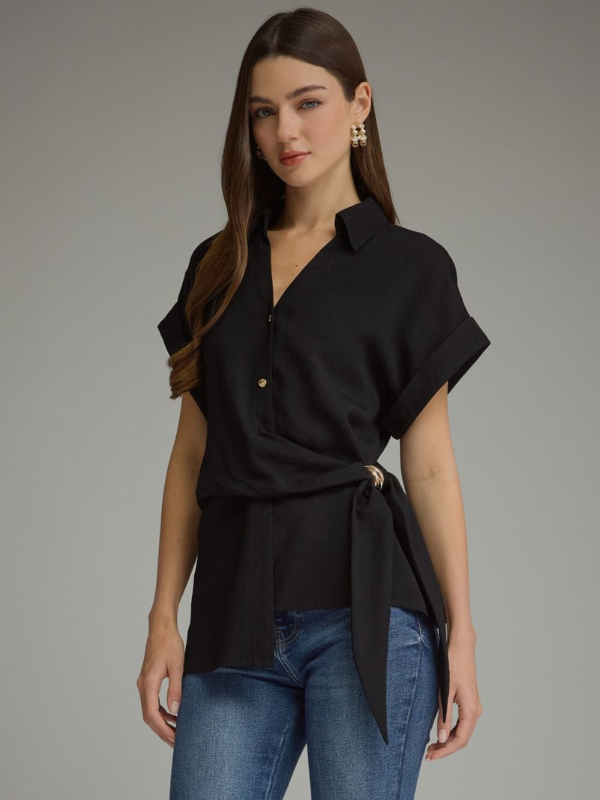 A woman modeling a black short-sleeve wrap-style blouse with a tie waist, paired with blue jeans, against a plain gray studio background.