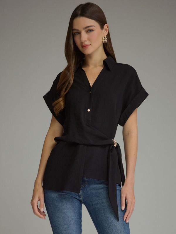 A woman modeling a black short-sleeve wrap-style blouse with a tie waist, paired with blue jeans, against a plain gray studio background.