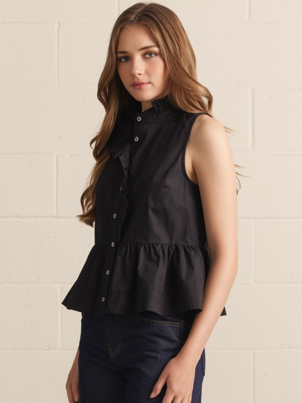 Woman wearing a black sleeveless blouse with ruffled details against a beige wall.