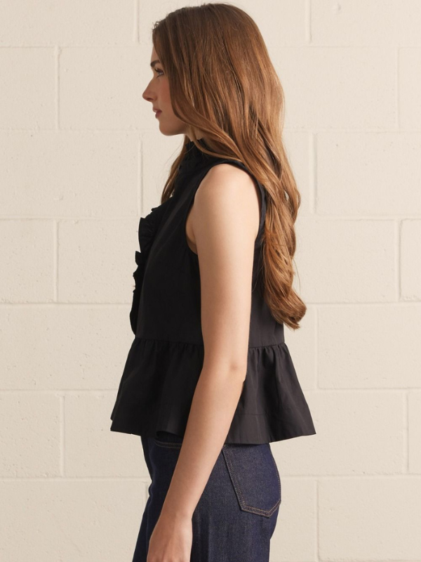 Woman wearing a black sleeveless peplum top against a beige tiled wall.