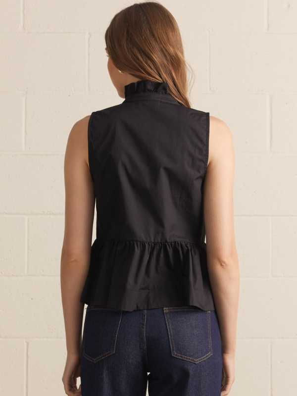 Woman wearing a black sleeveless top with a textured beige wall background