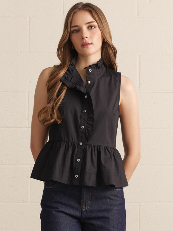 Woman wearing a black sleeveless blouse with ruffled details against a beige wall.