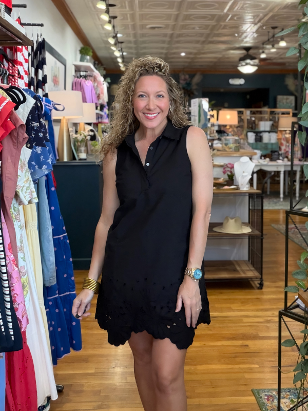 Woman in a black dress standing in a store with clothing racks and products in the background.