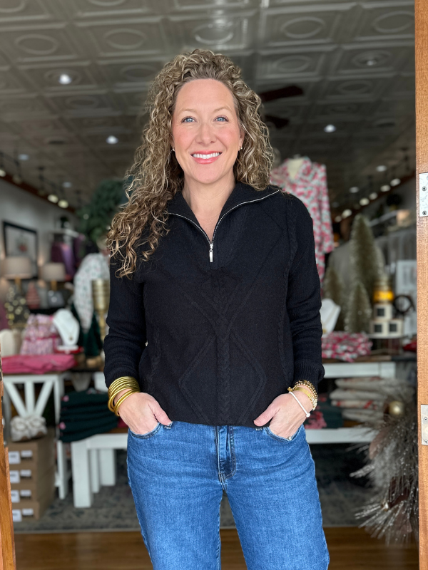 Woman wearing a black jacket and blue jeans standing in a store.