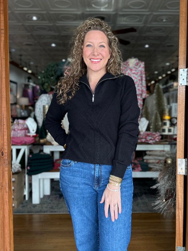 Woman standing in a store doorway wearing a black sweater and blue jeans.
