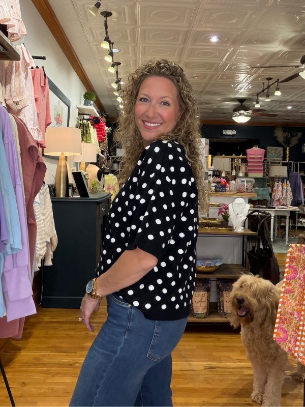 Woman in a polka dot shirt standing in a store with a dog.