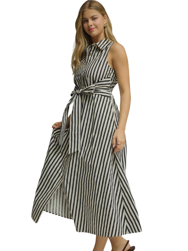 A woman modeling a sleeveless midi dress with vertical black and white stripes, featuring a tie waist and a high-low hemline, set against a plain white background.