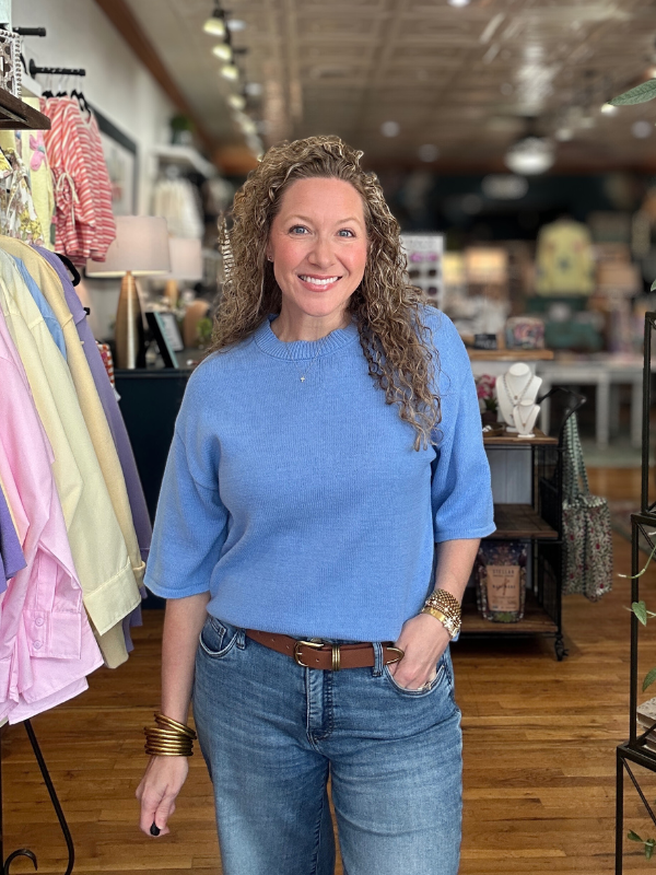 Woman wearing a blue sweater and jeans standing in a clothing store.