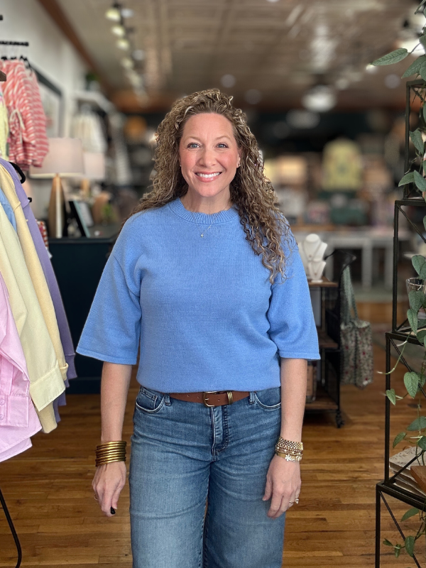 Woman wearing a blue sweater and jeans standing in a store.