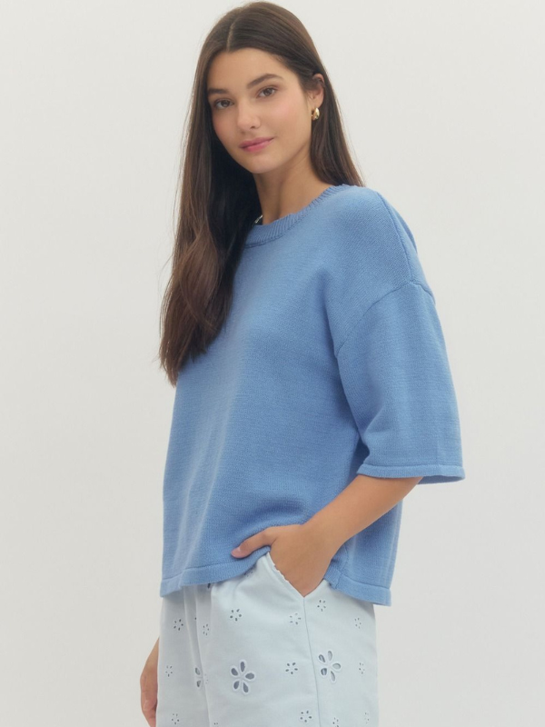 Woman wearing a blue oversized shirt with light-colored pants on a plain background