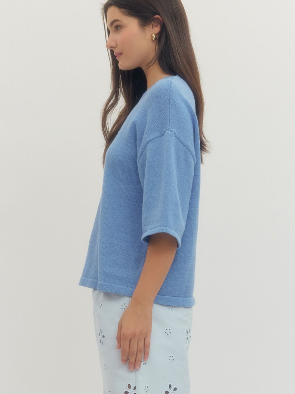 Woman wearing a blue top and light-colored pants against a plain background