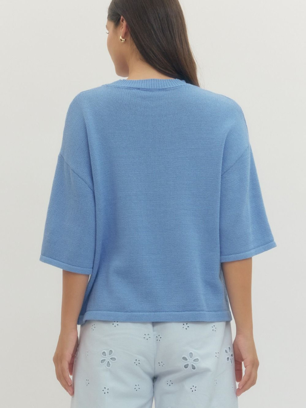 Person wearing a blue sweater and light-colored pants on a plain background