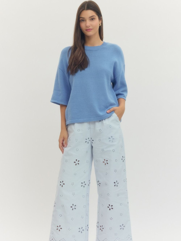 Woman wearing a blue sweater and light blue floral pants on a white background