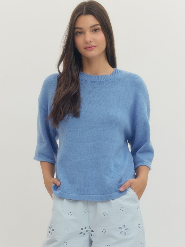 Woman wearing a blue sweater and light blue pants against a white background