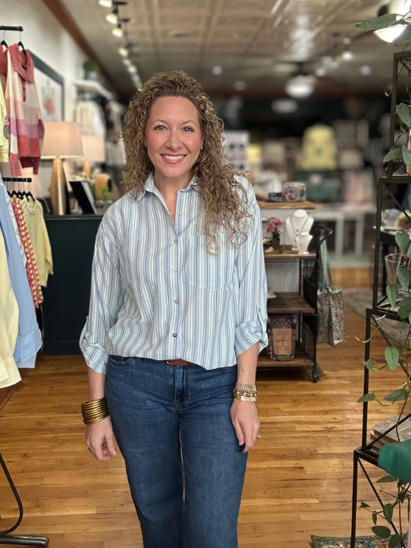 Woman standing in a clothing store wearing a striped shirt and jeans.