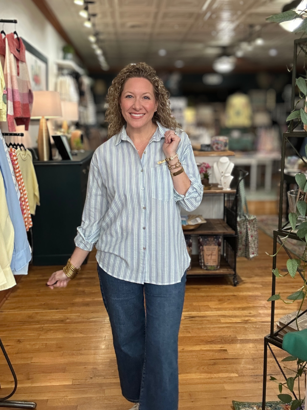 Woman standing in a clothing store wearing a striped shirt and jeans.
