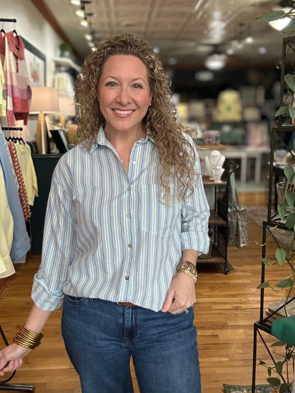 Woman standing in a store wearing a striped shirt and jeans, smiling.