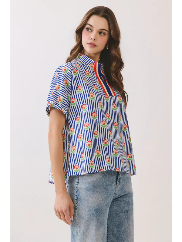 Woman wearing a colorful striped shirt with floral patterns on a plain background