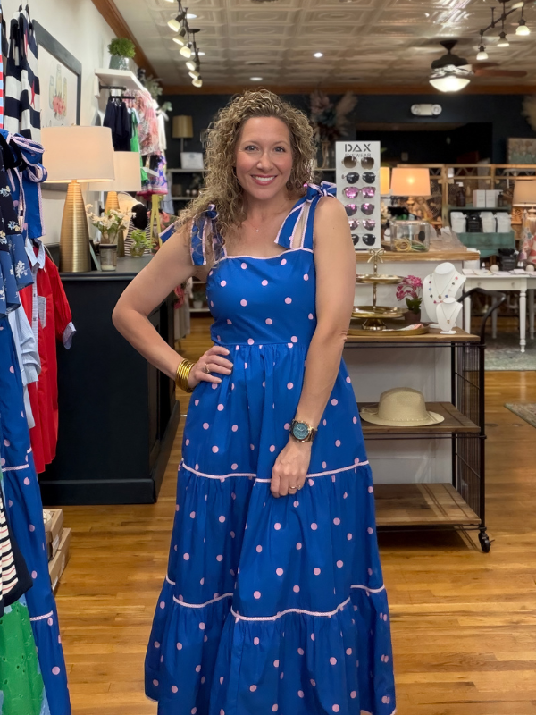 Woman in a blue polka dot dress standing in a store with various items in the background.