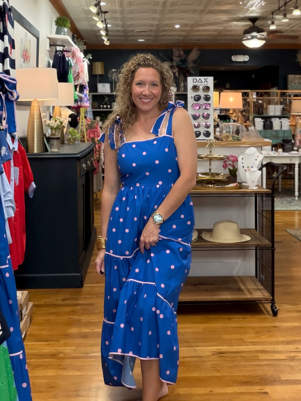 Woman in a blue polka dot dress standing in a store with various items on display.