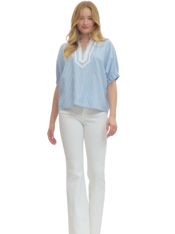Woman wearing a blue and white striped shirt with a white collar and white pants on a white background