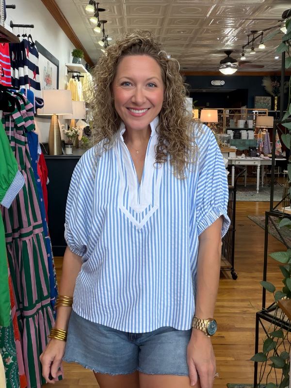 Woman wearing a blue and white striped shirt and denim shorts in a store setting.