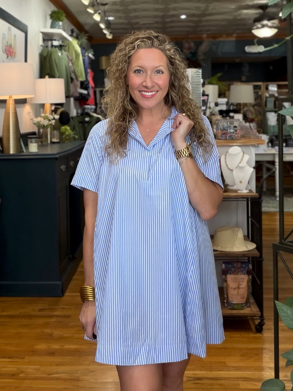 A woman with curly blonde hair wearing a light blue and white vertically striped short-sleeve shirt dress, standing in a retail store.